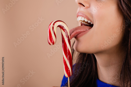 beautiful woman with christmas hoop licking candy cane isolated over brown