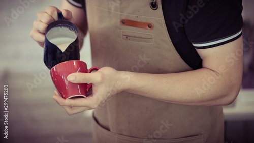 professional barista pouring streamed milk to make latte art in red cup of hot coffee, retro tone