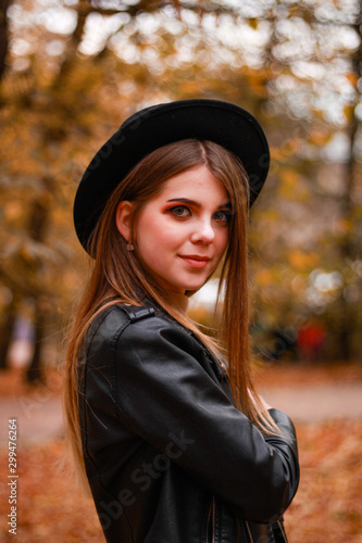 Stylish autumn girl in the park. Sweater, hat and leather jacket and leather skirt. Atmosphere. Makeup