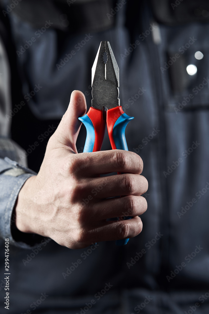Professional worker in overalls shows pliers on a dark background