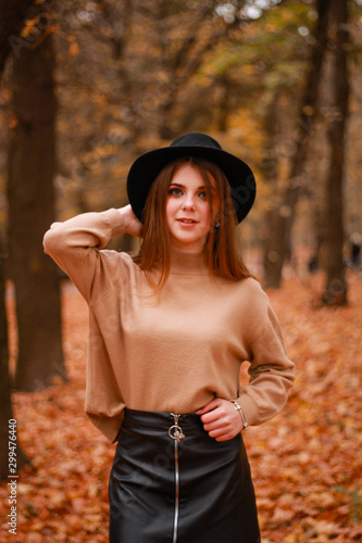 Autumn girl in the park. Sweater  hat and leather skirt. Stylish image. Atmosphere. Makeup