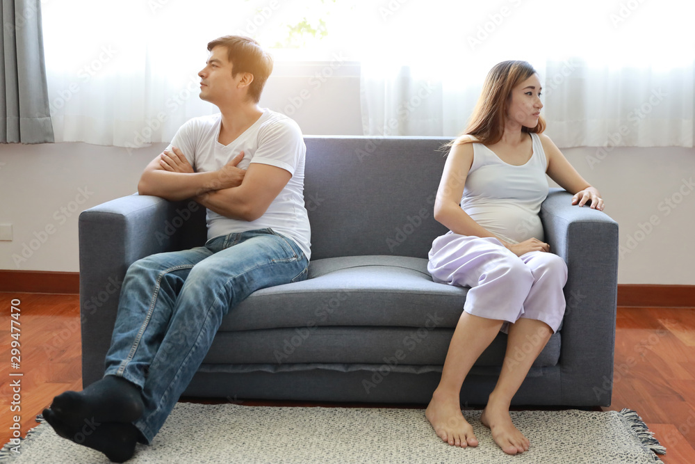 full shot asian pregnant wife and caucasian husband sitting on sofa in living room with angry motion with each other and unhappy face full shot asian pregnant wife and caucasian husband sitting on sofa in living room with angry motion with each other and unhappy face
