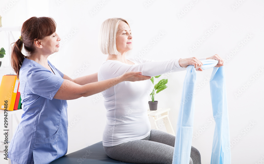 Physiotherapist and woman sitting on a bed exercising with a rubber tape
