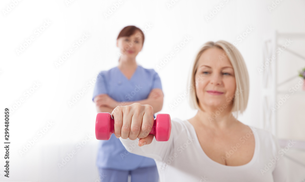Picture of middle aged woman during rehabilitation in professional clinic. Rehabilitation, physiotherapy with dumbbells Picture of middle aged woman during rehabilitation in professional clinic. Rehabilitation, physiotherapy with dumbbells