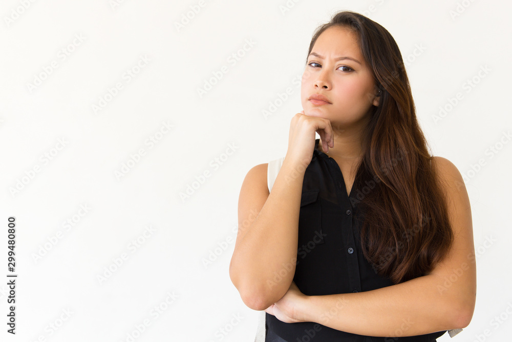 Serious woman with hand on chin looking at camera. Beautiful young woman standing with hand on chin and looking at camera isolated on white background. Facial expression concept Serious woman with hand on chin looking at camera. Beautiful young woman standing with hand on chin and looking at camera isolated on white background. Facial expression concept
