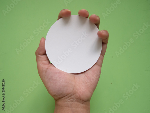 Woman hand holding white circle paper. Isolated in green background.