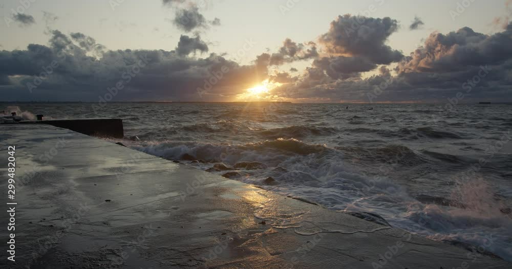 Storm waves rolling and splashing to the pier at sunset Storm waves rolling and splashing to the pier at sunset