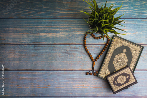 Flat lay view of vase, tasbih or rosary beads and Holy book of Quran with arabic calligraphy meaning of Al Quran over wooden paper background. Selective focus and crop fragment photo