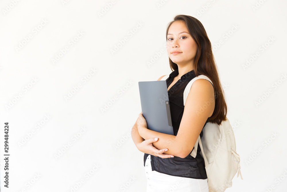 Confident young woman with folder and backpack. Portrait of beautiful serious young female student with backpack holding folder and looking at camera. Education concept Confident young woman with folder and backpack. Portrait of beautiful serious young female student with backpack holding folder and looking at camera. Education concept