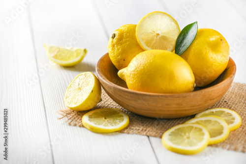 Fresh ripe yellow lemon in wooden bowl with green leaf on white table.  Healthy slices fruits on rustic board.