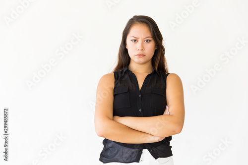 Frowning dissatisfied female customer looking at camera with arms folded. Young Latin woman in casual standing isolated over white background. Negative feedback concept