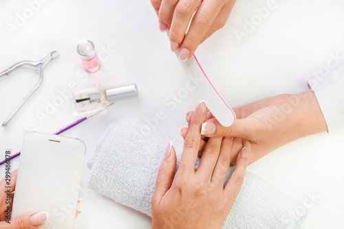 Woman receinving nails manicure with file in cosmetics salon. Beautiful nail care aftrer procedure top view.