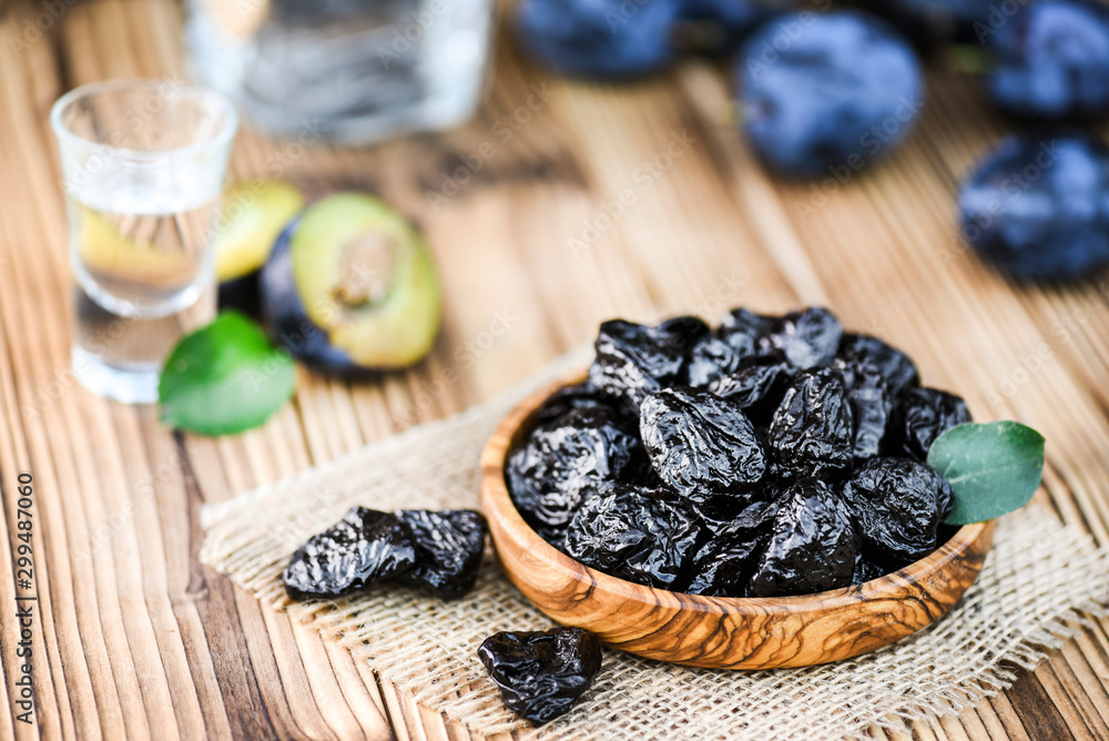 Prunes in bowl and green leaf. Slivovitz or alcohol brandy bottle and small glass with fresh plume in background. Prunes in bowl and green leaf. Slivovitz or alcohol brandy bottle and small glass with fresh plume in background.