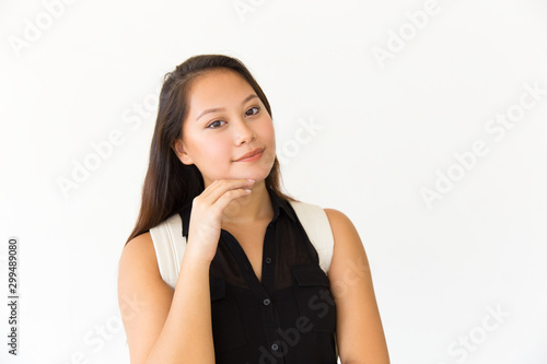 Positive satisfied student girl touching facial skin and looking at camera. Young Latin woman in casual standing isolated over white background, smiling. Skincare concept © Mangostar