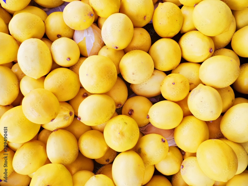 Bright yellow lemons close-up. Citrus fruits on counter of greengrocery. Drops of water on lemon peel. Selective focus image.
