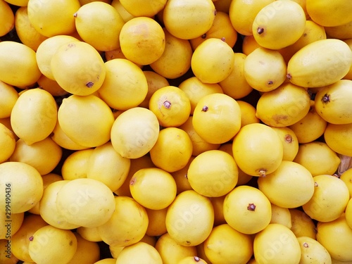 Bright yellow lemons close-up. Citrus fruits on counter of greengrocery. Drops of water on lemon peel. Selective focus image.