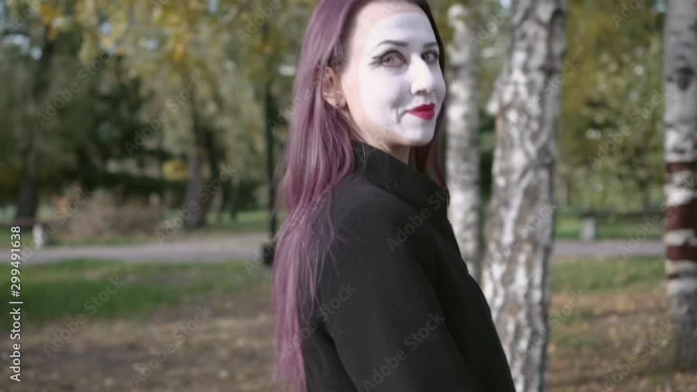 Mime girl in a black coat walking along a city street looked around greeted or said goodbye with a hand. Mime girl in a black coat walking along a city street looked around greeted or said goodbye with a hand.