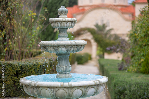 White three-tiered fountain with azure interior paint in the middle of the garden.