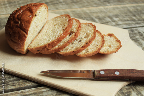  On a wooden board lies bread sliced. Nearby lies a knife.