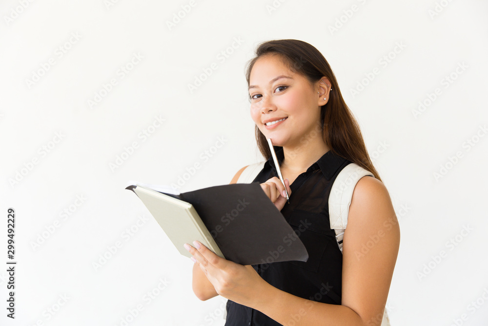 Happy joyful student girl studying her notes, holding pen and open notebook, looking at camera. Young Latin woman standing isolated over white background. Education concept Happy joyful student girl studying her notes, holding pen and open notebook, looking at camera. Young Latin woman standing isolated over white background. Education concept