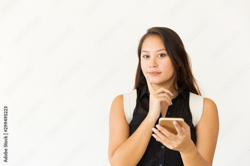 Young woman with smartphone smiling at camera. Portrait of beautiful thoughtful young female student with backpack using mobile phone on white background. Technology concept Young woman with smartphone smiling at camera. Portrait of beautiful thoughtful young female student with backpack using mobile phone on white background. Technology concept