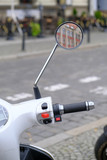 Urban white scooter is parked on cobblestone road in a tourist center of the city. Handle controls, mirror with reflection of an old house close-up.