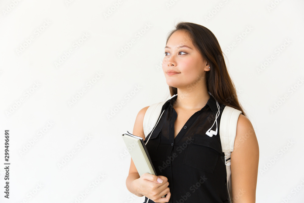 Positive college student wearing backpack, holding copybooks, looking away. Young Latin woman standing isolated over white background. Advertising concept Positive college student wearing backpack, holding copybooks, looking away. Young Latin woman standing isolated over white background. Advertising concept