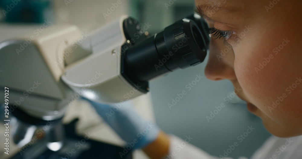 Portrait of blond female scientist is analyzing a sample to extract the DNA and molecules with microscope in laboratory.