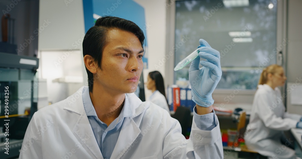 Portrait of Chinese male scientist is analyzing a liquid to extract the DNA and molecules in the test tubes in laboratory.