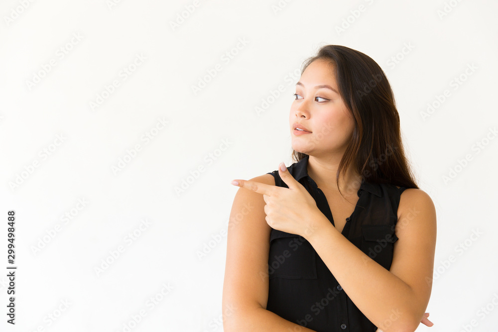 Curious young woman pointing away. Beautiful young woman pointing aside with finger and looking at copy space. Gesture concept Curious young woman pointing away. Beautiful young woman pointing aside with finger and looking at copy space. Gesture concept