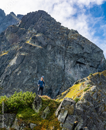 A woman (tourist) in a helmet on a grassy rock ridge in the mountains on the background of the peaks.