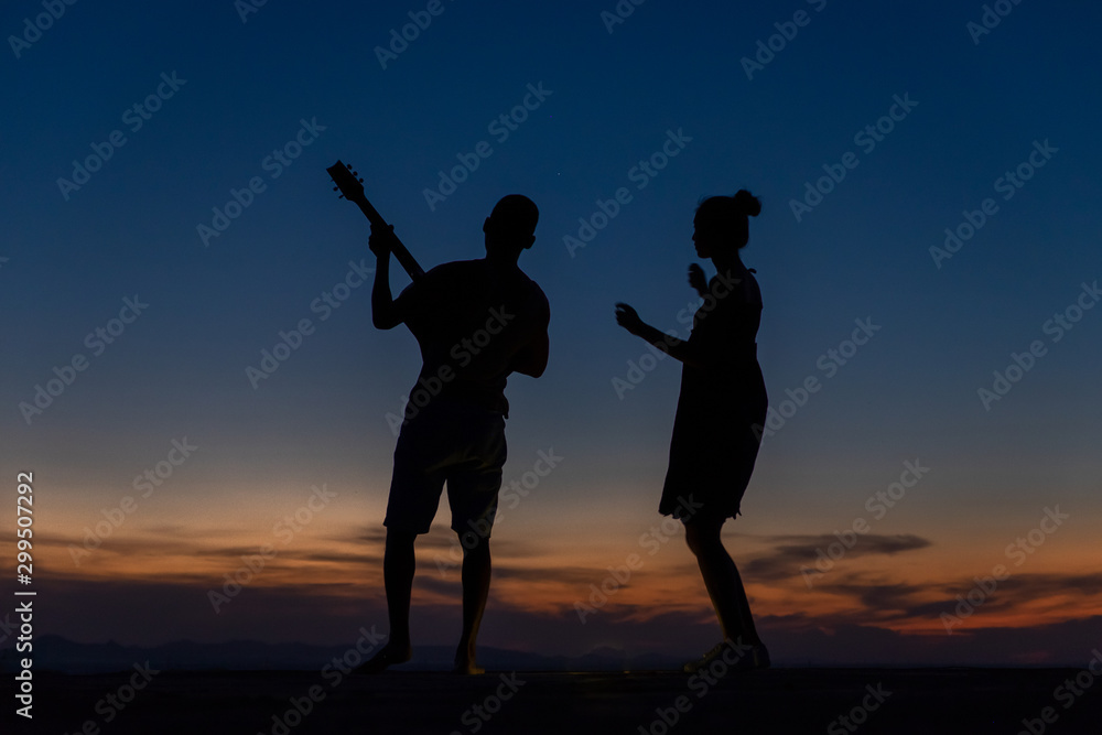 A silhouette of a happy young couple slow dancing outside at sunset, with copy-space in sky.