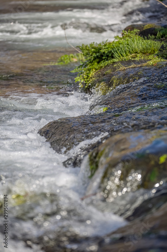 View of small waterfall on river with detail of water foam, rocks and river vegetation