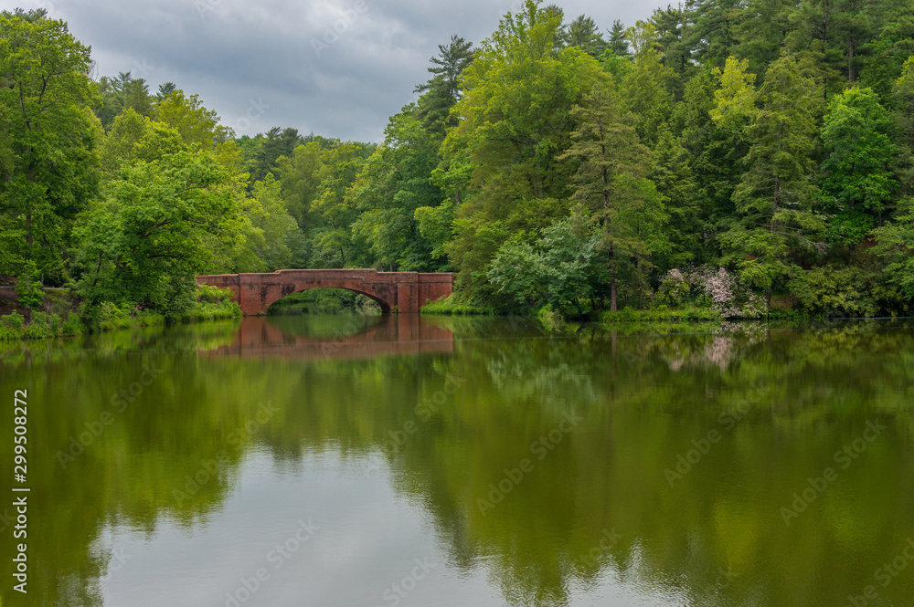 Stone walk bridge on lake in the park. Trees reflecting water 