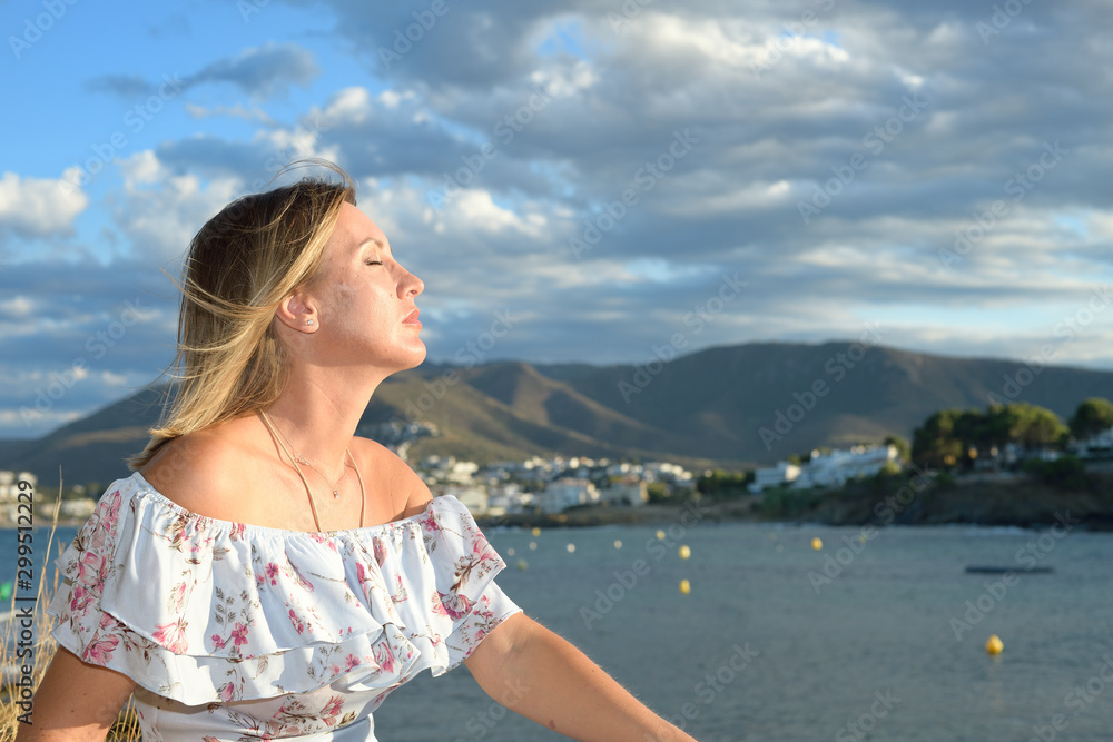 Portrait of a woman sitting in front of a coastal landscape of the northern mediterranean on a summer afternoon with wind taking a sunbath with copy space