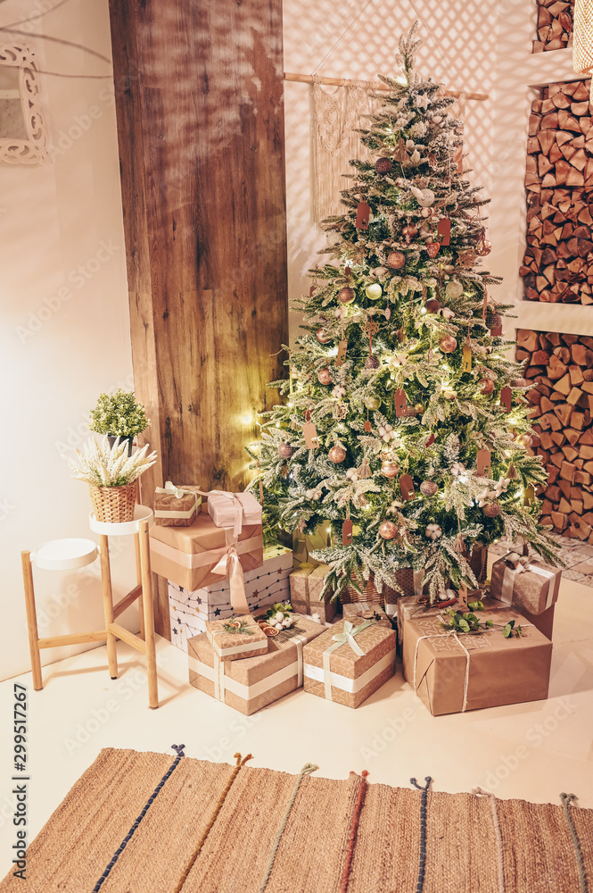 New year winter home interior. Christmas tree holiday decorations, firewood, eco gift boxes made with craft paper. White stylish cozy scandinavian style living room. Festive home night  muffled light
