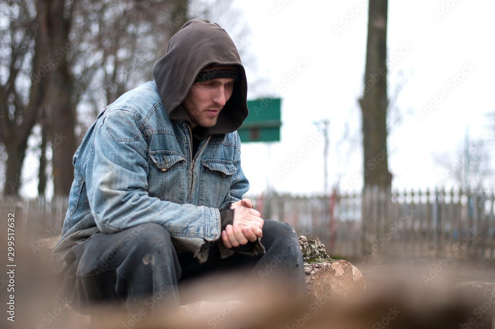 Homeless, sad man in a beanie sitting outside and feeling cold, trying to warm up his hands Homeless, sad man in a beanie sitting outside and feeling cold, trying to warm up his hands
