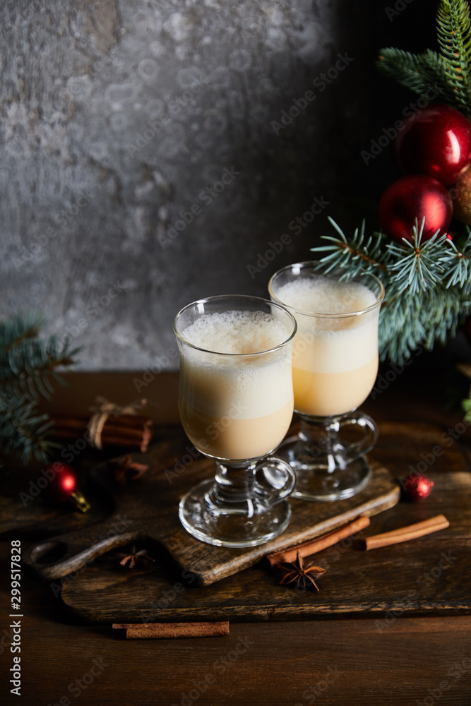 traditional eggnog cocktail on cutting board near decorated spruce branches on grey stone background traditional eggnog cocktail on cutting board near decorated spruce branches on grey stone background