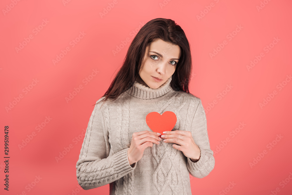 attractive woman in sweater holding heart-shaped paper cut on pink attractive woman in sweater holding heart-shaped paper cut on pink
