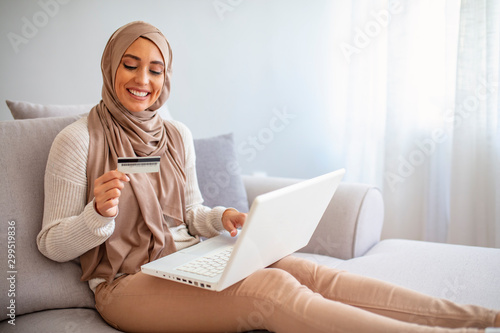 Elegant attractive muslim woman using mobile laptop searching online shopping information in living room at home. Portrait of happy woman purchasing product via online shopping. pay using credit card