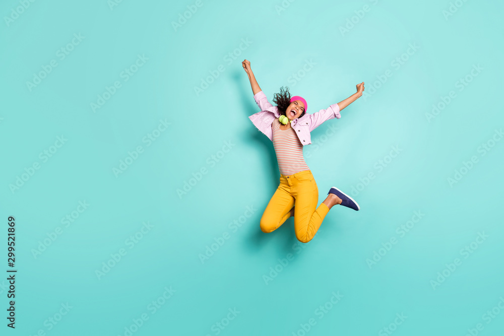 Fototapeta premium Full length body size photo of overjoyed ecstatic rejoicing girl causal jumping screaming in striped t-shirt pink jacket cap headwear yellow trousers isolated vivid color background turquoise