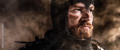 Fotografia, Obraz panoramic shot of handsome knight in armor looking away on black background
