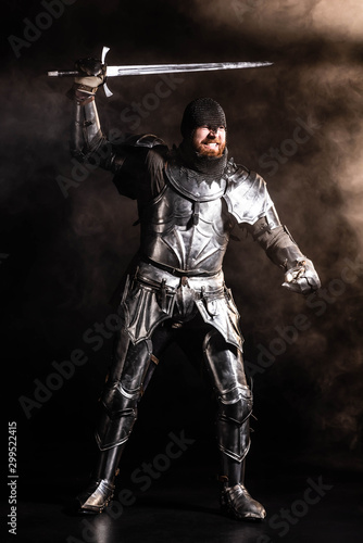 handsome knight in armor holding sword and fighting on black background