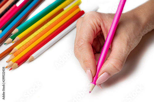 hand holds the colored pencil, in the background a lot of colored pencils