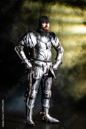 handsome knight in armor looking away with hands on hips on black background © LIGHTFIELD STUDIOS