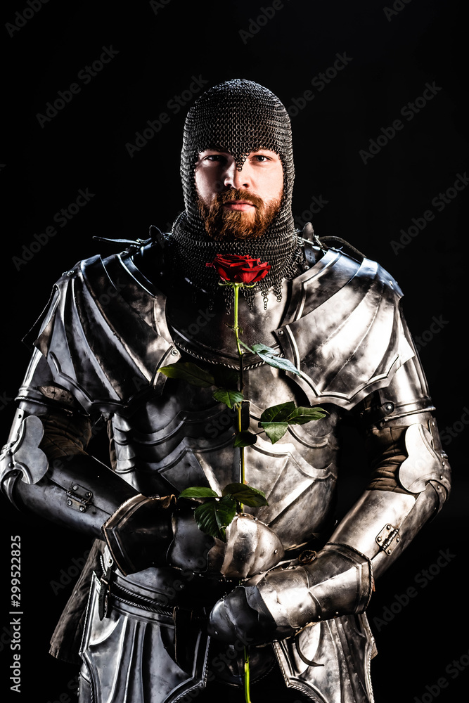 handsome knight in armor holding rose isolated on black
