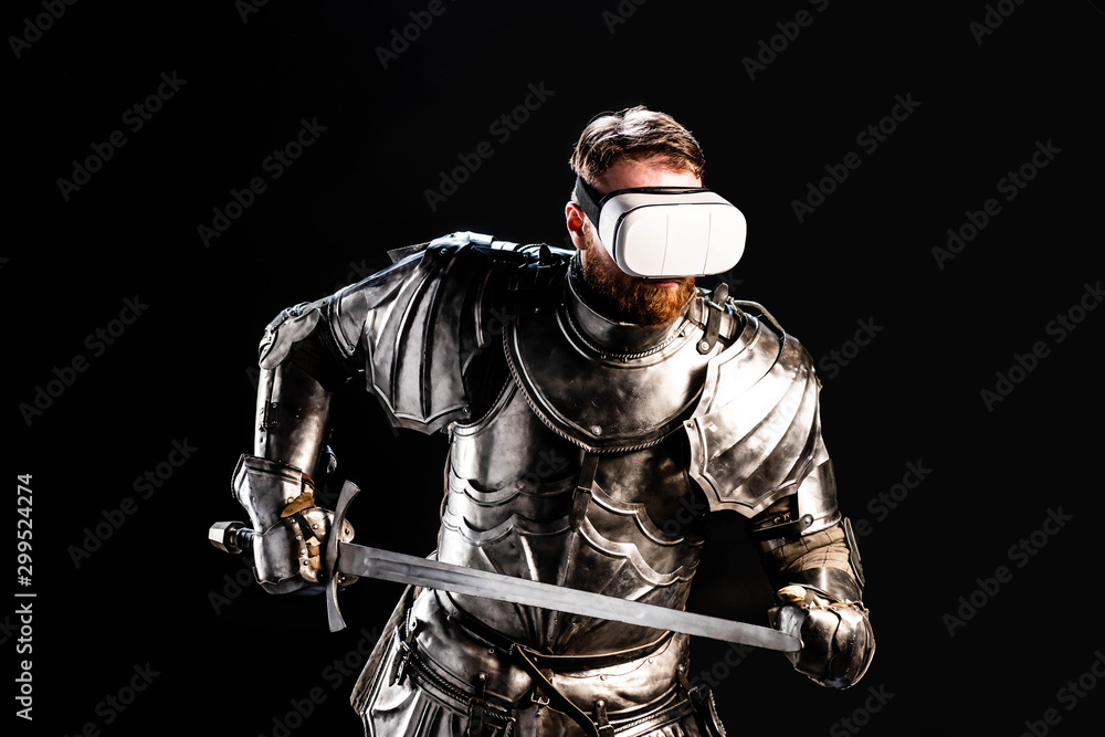 Naklejka premium knight with virtual reality headset in armor holding sword isolated on black