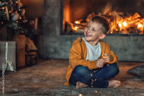 The boy sits under the Christmas tree on the background of New Year's lights