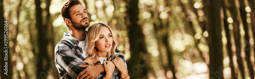 panoramic shot of happy man embracing attractive girlfriend while looking away in park