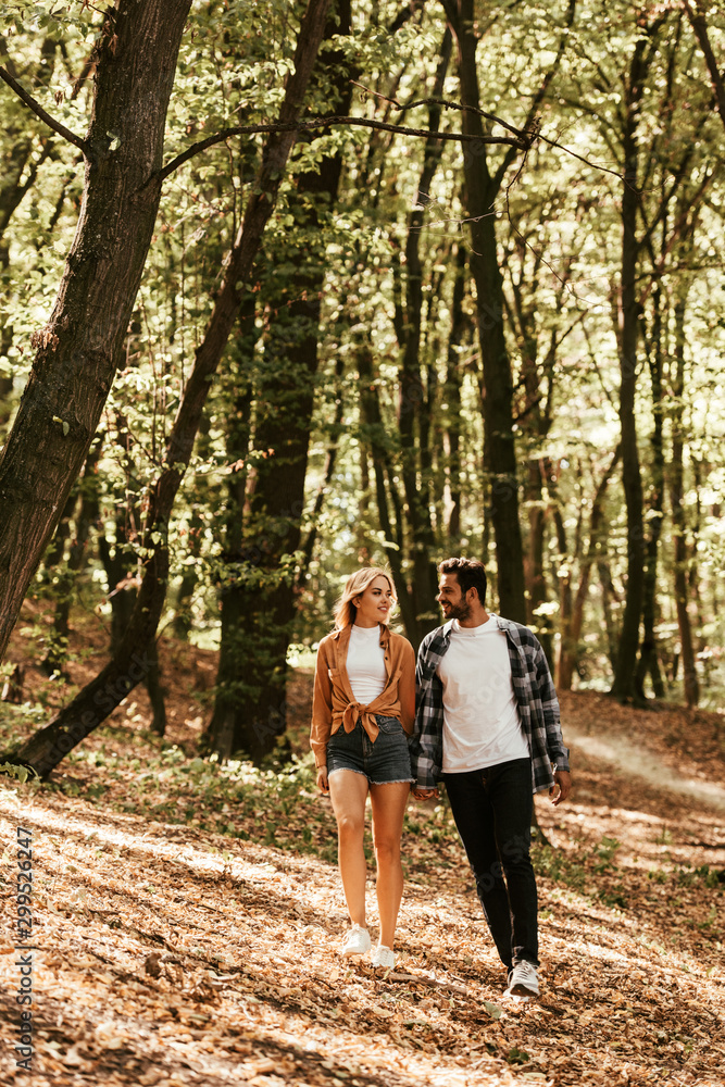 smiling young couple holding hands and looking at each other while walking in park smiling young couple holding hands and looking at each other while walking in park